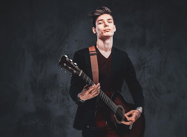 Un joven atractivo toca la guitarra acústica en el estudio mientras posa para el fotógrafo.