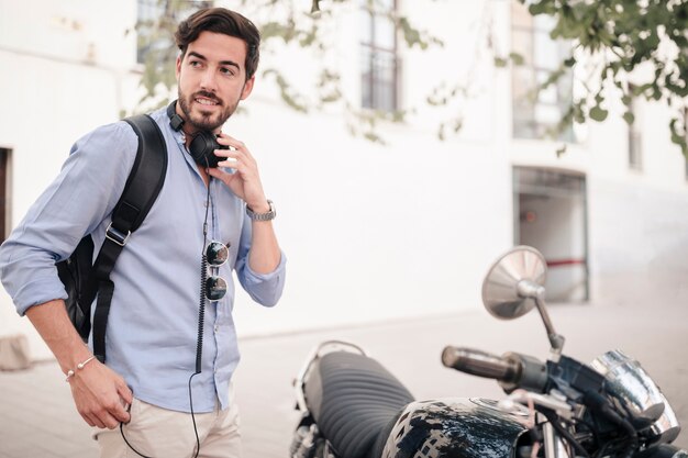 Joven con auriculares de pie cerca de la moto