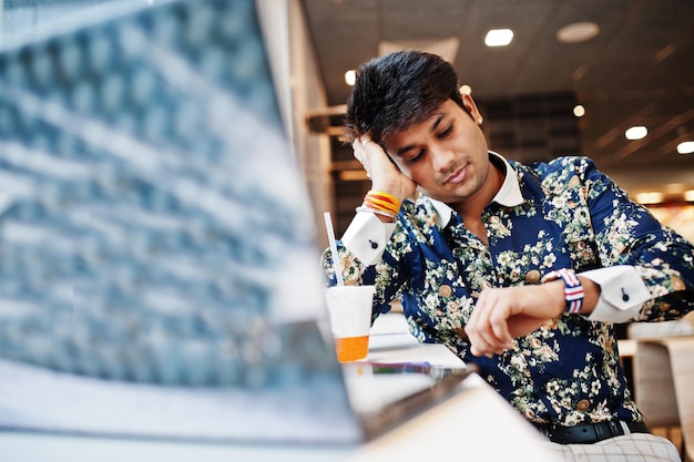 Joven autónomo indio sentado con una computadora portátil abierta en un café de comida rápida un hombre asiático guapo mirando relojes durante el trabajo en un netbook en una cómoda cafetería