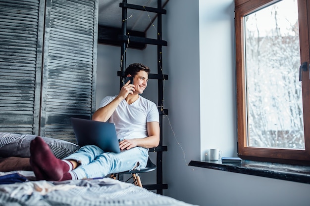 Foto gratuita joven autónomo trabajando en una computadora portátil y hablando con alguien en apartamentos de lujo