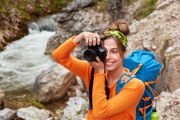 Joven aventurera posa contra un pequeño río en el barranco, sostiene la cámara