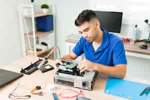 Foto gratuita joven averiguando si la conexión funciona. técnico hispano conectando un nuevo disco duro en una computadora y revisando el hardware