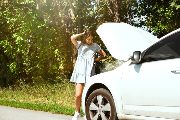 La joven averió el coche mientras viajaba camino de descansar. Ella está tratando de arreglar el daño por su cuenta o debería hacer autostop. Poniéndose nervioso. Fin de semana, problemas en la carretera, vacaciones.