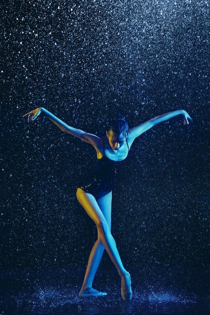 Joven bailarina de ballet actuando bajo gotas de agua y spray. Modelo caucásico bailando en luces de neón. Mujer atractiva. Concepto de ballet y coreografía contemporánea.