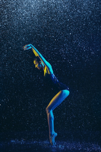 Joven bailarina de ballet actuando bajo gotas de agua y spray. Modelo caucásico bailando en luces de neón. Mujer atractiva.