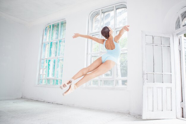 Joven bailarina de ballet moderno saltando sobre la pared blanca