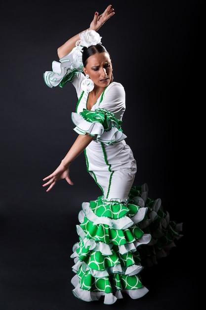 Joven bailarina de flamenco en hermoso vestido sobre fondo negro.