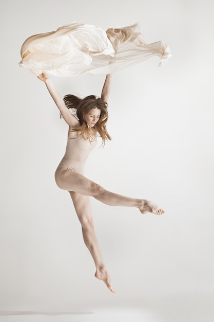 Joven bailarina hermosa en traje de baño beige bailando en gris