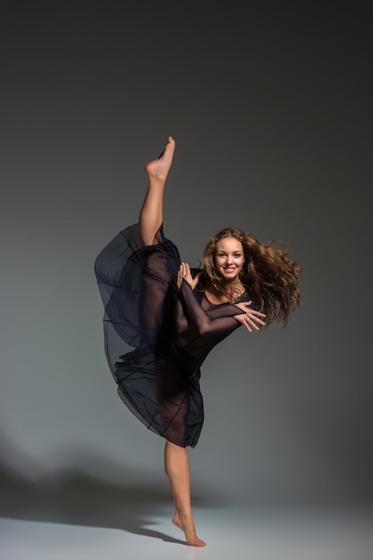 Joven bailarina hermosa vestida de negro posando sobre un fondo de estudio gris oscuro. Moderno, Contemporáneo, improvisación