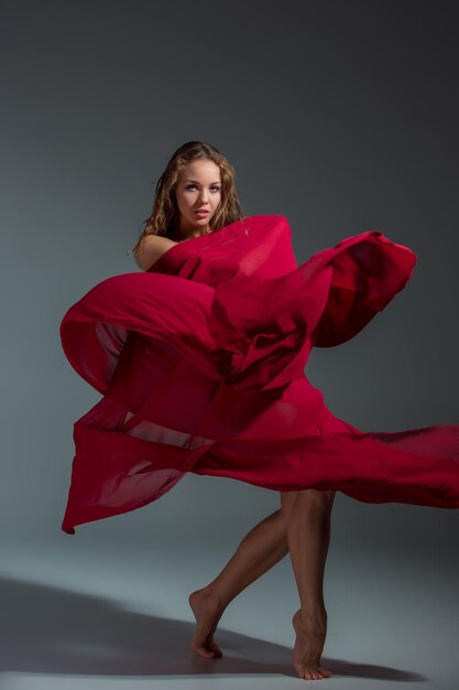 Joven bailarina hermosa con vestido rojo posando sobre un fondo de estudio gris oscuro. Moderno, Contemporáneo, improvisación