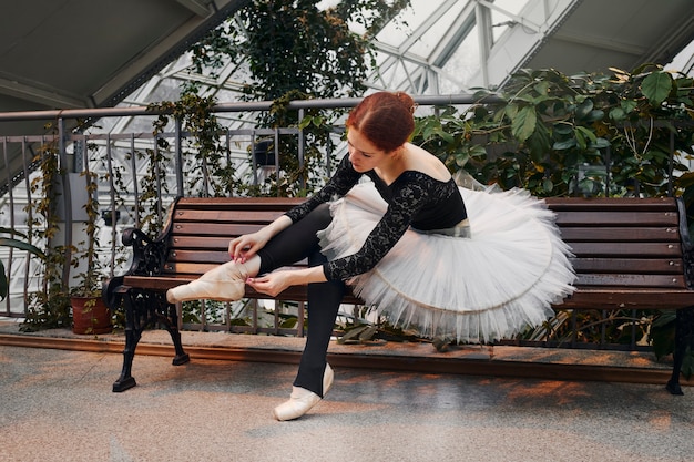 Joven bailarina poniéndose sus zapatillas de punta en un jardín botánico interior