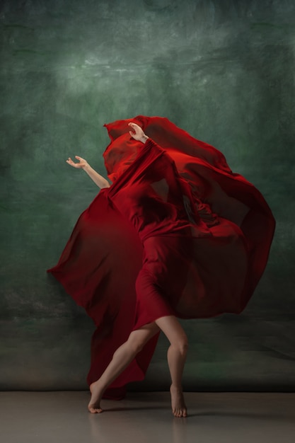 Joven bailarina tierna elegante en espacio de estudio verde oscuro con tela roja