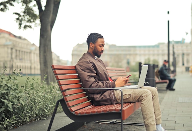 joven en un banco con una computadora y un teléfono inteligente