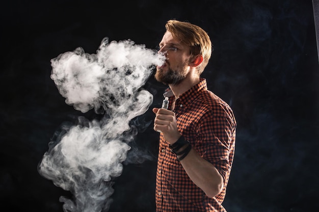 Un joven con barba y un peinado elegante en una camisa, fumando un cigarrillo, una víbora, una habitación, un estudio, humo, disfrute. Fondo negro