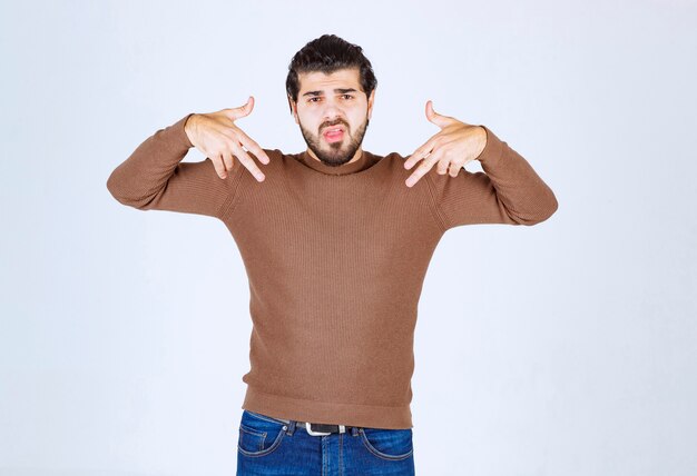 joven con barba de pie y apuntando a sí mismo.