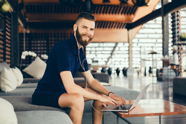 un joven con barba trabaja en un café, un profesional independiente usa una computadora portátil, hace un proyecto