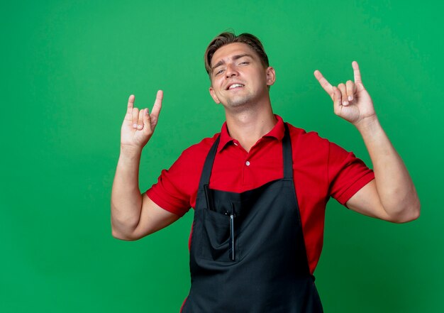 Joven barbero masculino rubio seguro en gestos uniformes cuernos signo de mano