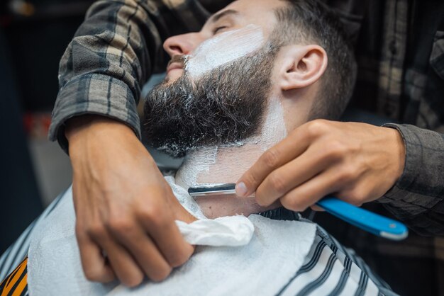 Joven barbudo afeitado por peluquero en barbería