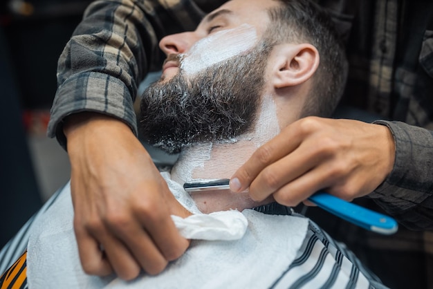 Joven barbudo afeitado por peluquero en barbería