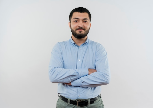 Foto gratuita joven barbudo con camisa azul con brazos cruzados sonriendo confiado