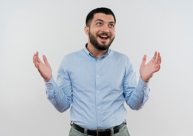 Joven barbudo con camisa azul levantando las manos feliz y emocionado