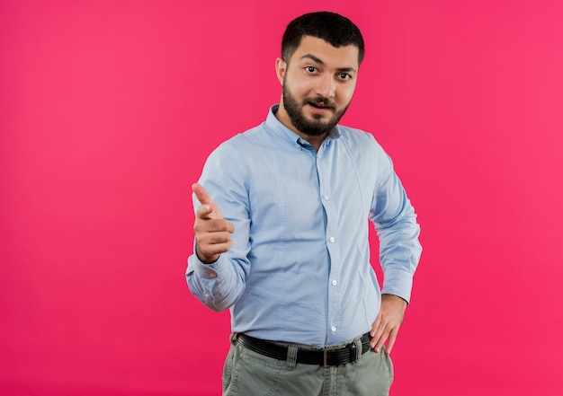 Joven barbudo con camisa azul sonriendo confiado apuntando a la cámara