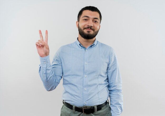 Joven barbudo con camisa azul sonriendo mostrando v-sign