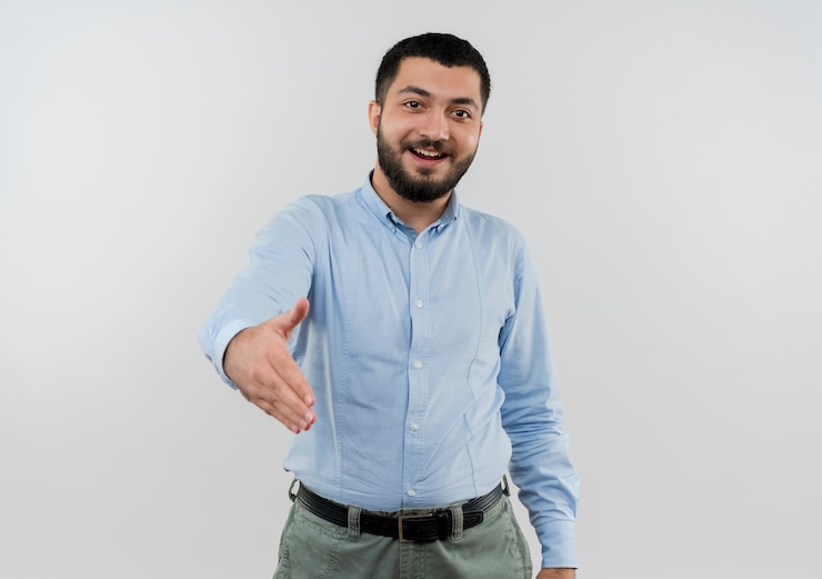 Foto gratuito joven barbudo con camisa azul sonriendo ofreciendo saludo de mano sonriendo amable