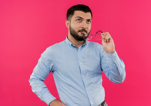 Foto gratuita joven barbudo con camisa azul sosteniendo vidrioso mirando desconcertado