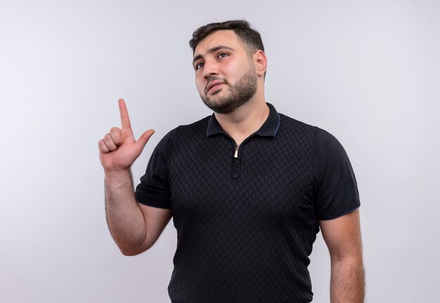 Joven barbudo con camisa negra apuntando con el dedo hacia arriba tratando de recordar