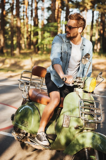 Joven barbudo concentrado sentado en scooter al aire libre