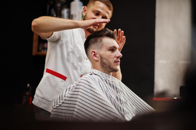 Joven barbudo cortándose el pelo con un peluquero mientras se sienta en una silla en la barbería