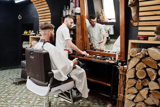 Joven barbudo cortándose el pelo con un peluquero mientras se sienta en una silla en la barbería