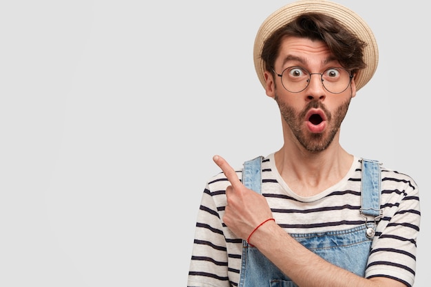 Joven barbudo con gafas redondas y overoles de mezclilla