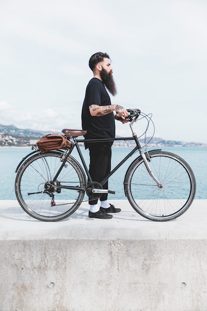 Joven barbudo hombre de pie con bicicleta en rompeolas