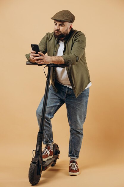 Joven barbudo montando scooter eléctrico y usando el teléfono