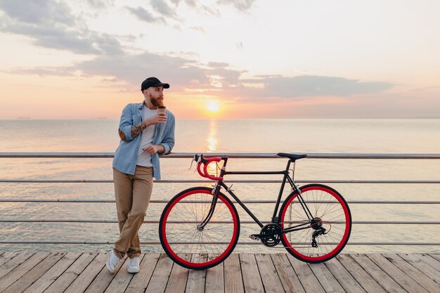 Joven barbudo viajando en bicicleta al mar al atardecer