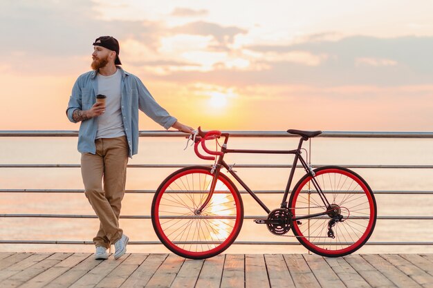 Joven barbudo viajando en bicicleta al mar al atardecer