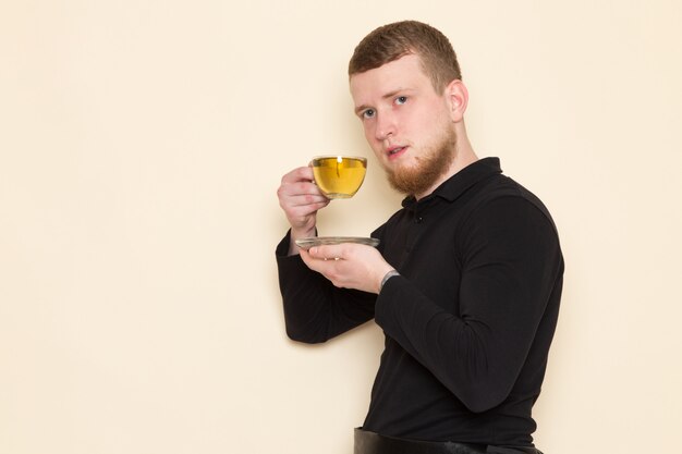 Joven barista en traje negro bebiendo té verde caliente en el escritorio blanco