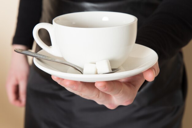 Joven barista en traje de trabajo negro con ingredientes y equipo de café semillas de café marrón sobre blanco