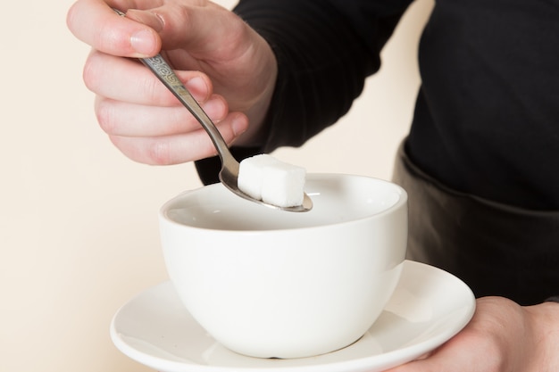 Joven barista en traje de trabajo negro con ingredientes y equipo de café semillas de café marrón sobre blanco