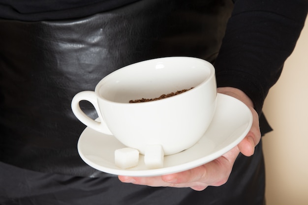 Foto gratuita joven barista en traje de trabajo negro con ingredientes y equipo de café semillas de café marrón sobre blanco