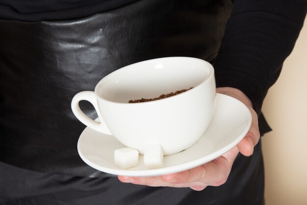 Joven barista en traje de trabajo negro con ingredientes y equipo de café semillas de café marrón sobre blanco