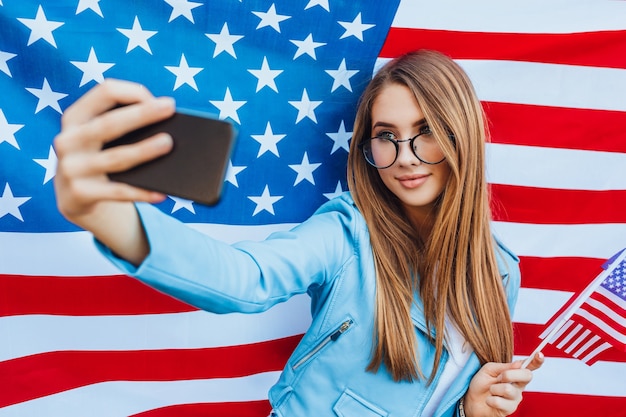 Joven bastante americana haciendo selfie con bandera americana.