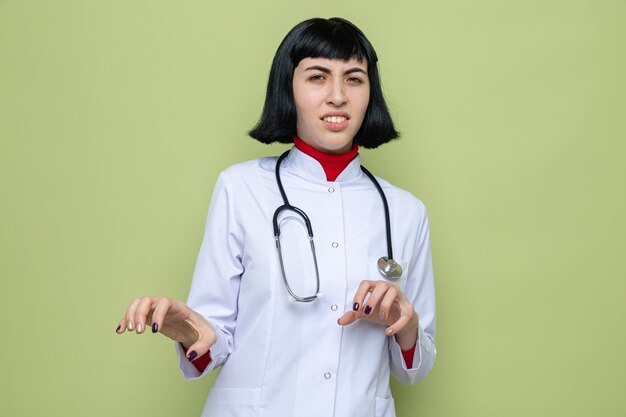 Joven bastante caucásica disgustada en uniforme médico con estetoscopio apretando sus dedos