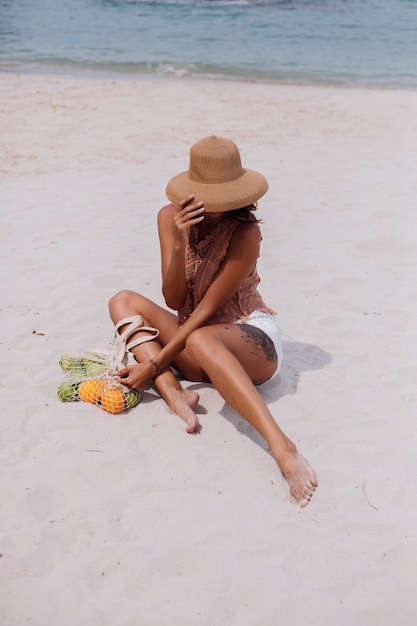 Joven bastante caucásica mujer en forma bronceada en ropa de punto y sombrero en la playa