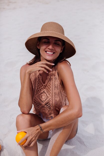 Foto gratuita joven bastante caucásica mujer en forma bronceada en ropa de punto y sombrero en la playa