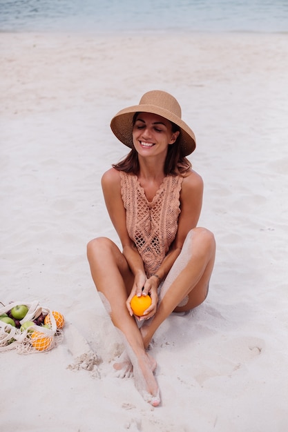 Joven bastante caucásica mujer en forma bronceada en ropa de punto y sombrero en la playa