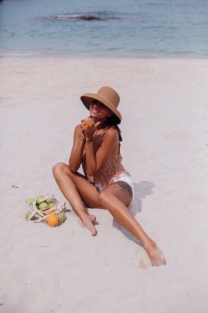 Joven bastante caucásica mujer en forma bronceada en ropa de punto y sombrero en la playa