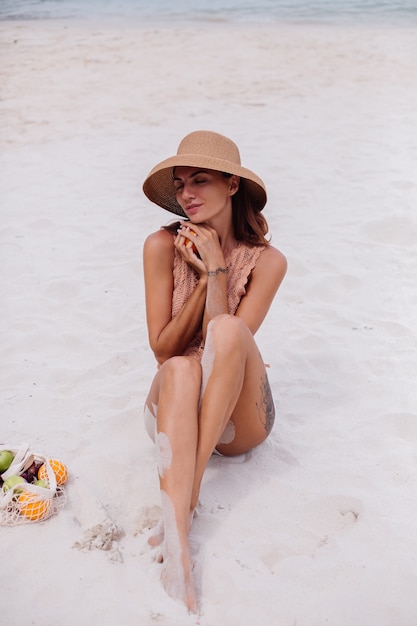 Joven bastante caucásica mujer en forma bronceada en ropa de punto y sombrero en la playa